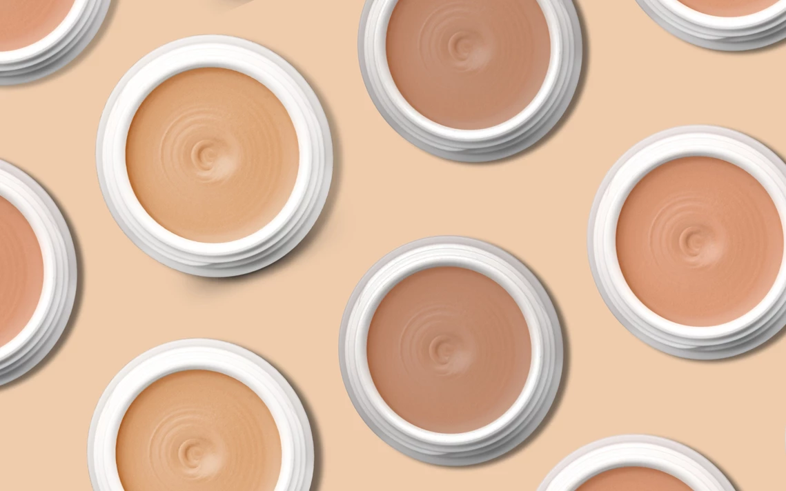 Verschiedene offene Tiegel mit Creme-Foundations in mehreren Hauttönen, präsentiert auf hellem Untergrund.